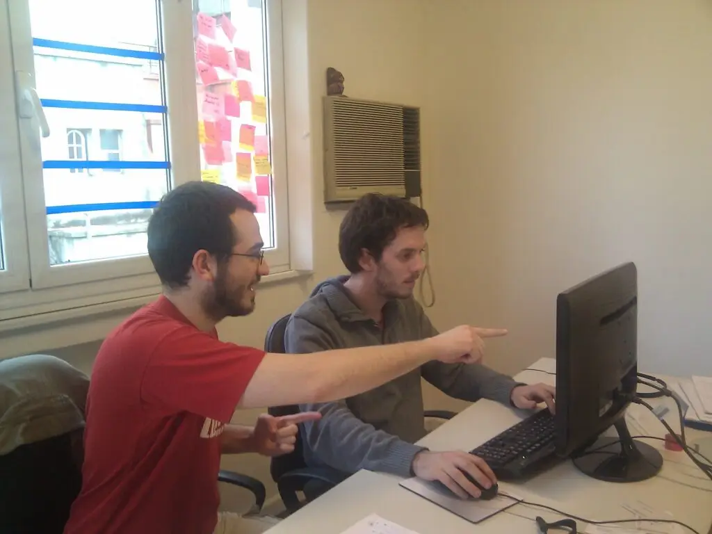 Dos programadores revisan código juntos en un ordenador; fotografía contextual.