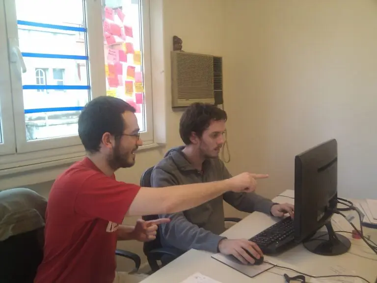 Dos programadores revisan código juntos en un ordenador; fotografía contextual.