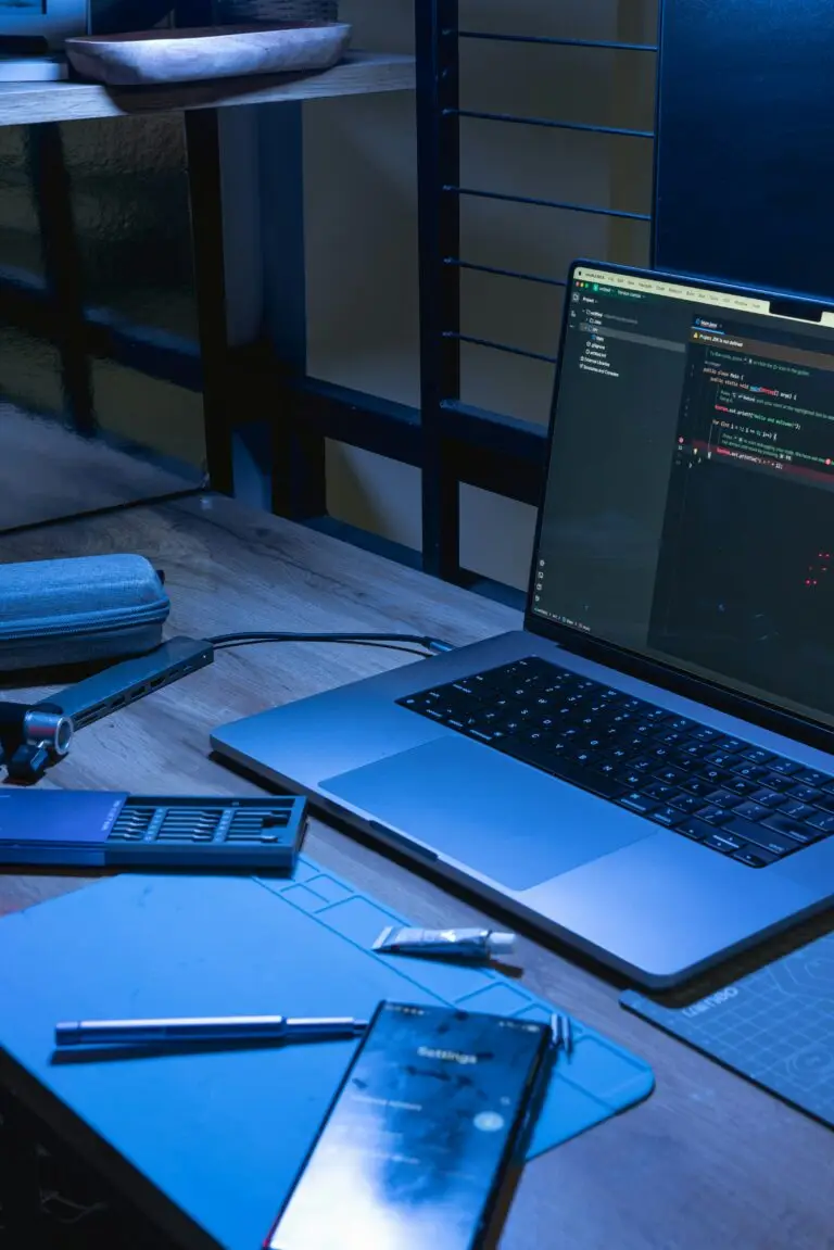 Portátil con código abierto y un teléfono sobre una mesa iluminada en azul