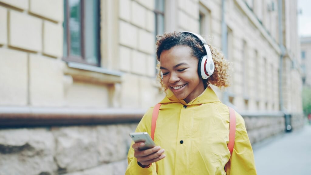 Mujer con chaqueta amarilla y auriculares mira su teléfono en una calle